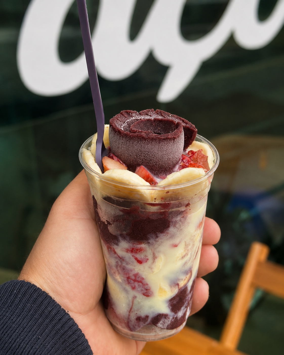 Copo de açaí Norte Sul segurado na mão, com banana, morango e rolo de açaí